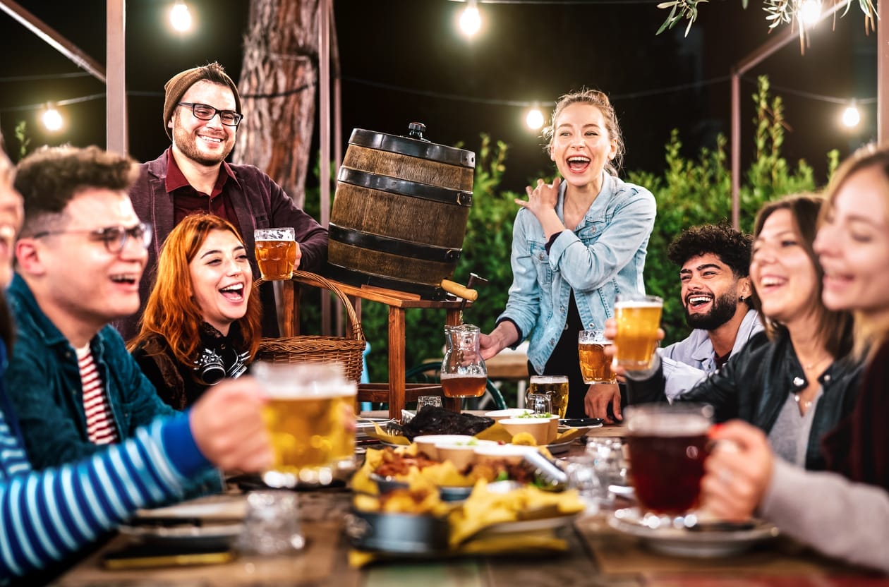 Happy Men And Women Having Fun Drinking Out At Beer Garden Social Gathering Life Style Concept On Young People Enjoying Hangout Time Together At Night Warm Filter With Shallow Depth Of Field